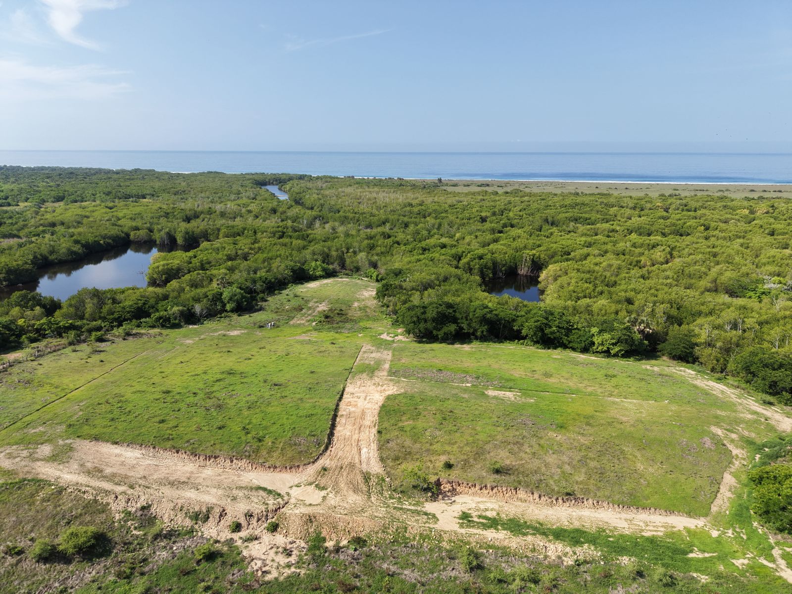 Fotografía aérea del terreno verde con su camino de acceso, junto a la laguna